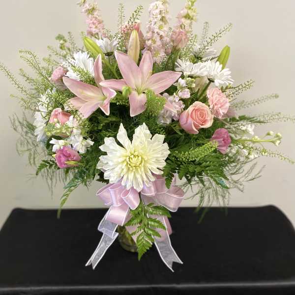 Pink lilies and white daisies in a glass vase with a pink ribbon