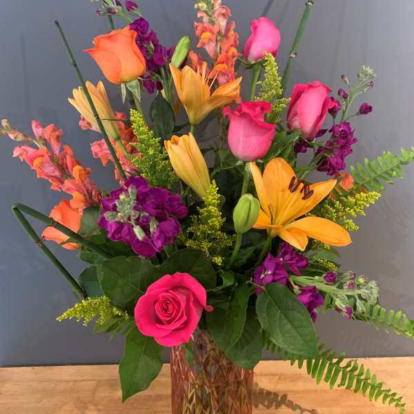 Mixed bouquet of roses, lilies, and purple blooms in a glass vase