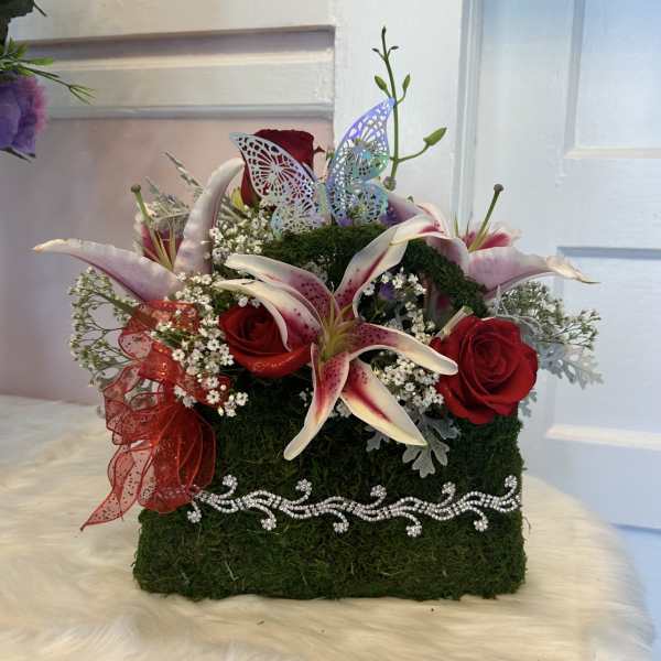 Red roses and pink lilies in a moss-covered box with a butterfly decoration