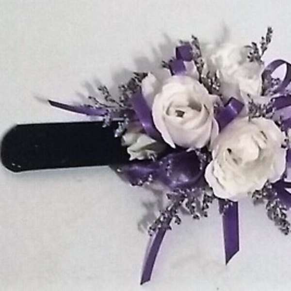 White floral wrist corsage with purple ribbon on a black band