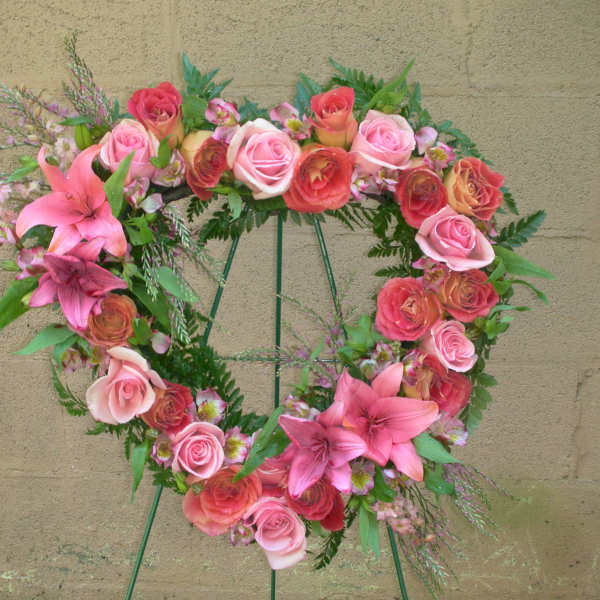 Heart-shaped floral wreath with pink roses and lilies on a stand