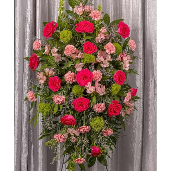 Standing spray of hot pink roses, pink carnations, and green mums on a metal easel.