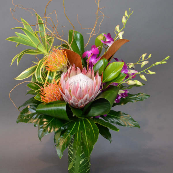 Tropical flower arrangement in a glass vase with pink protea and purple orchids