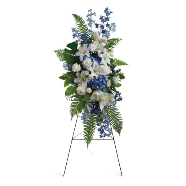 Standing floral spray with white lilies and blue flowers on a metal easel