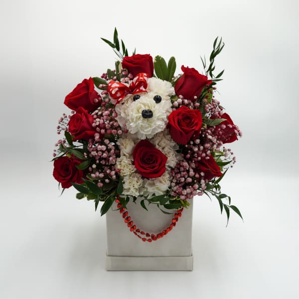 Red roses and white flowers arranged around a teddy bear in a box