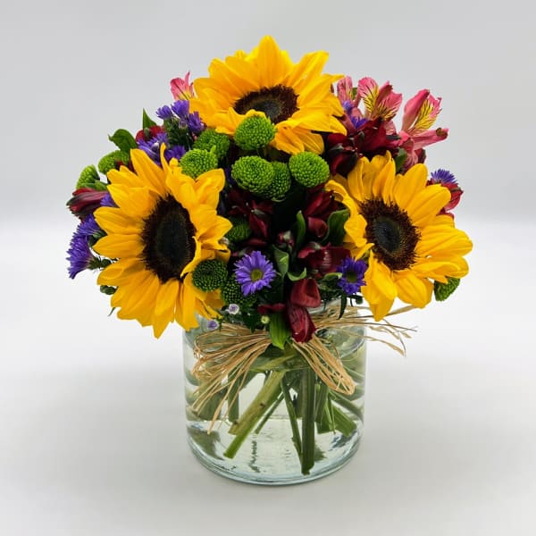 Sunflower bouquet in a clear glass vase with purple and burgundy flowers