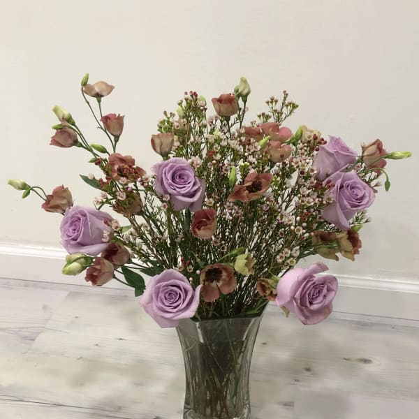 Lavender roses and small pink blooms in a clear glass vase
