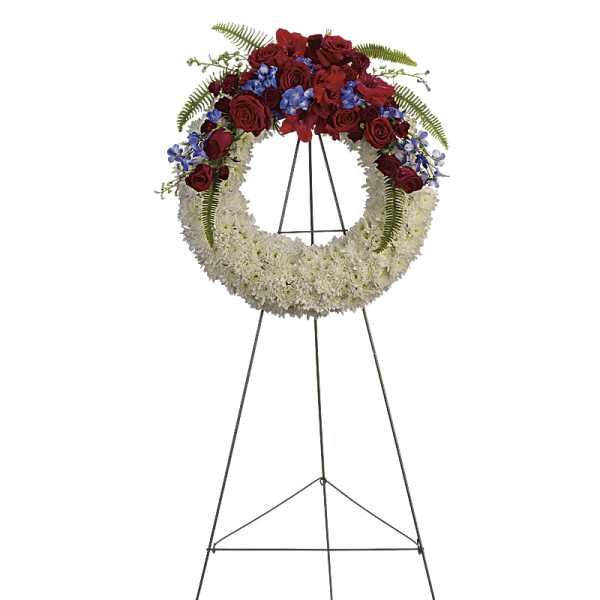Standing funeral wreath with red roses, white flowers, and blue accents on an easel