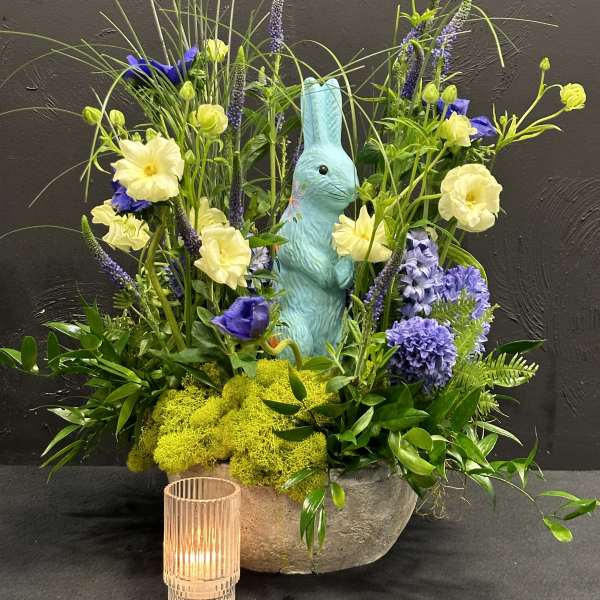 Spring floral arrangement with a blue bunny figurine and a small candle holder