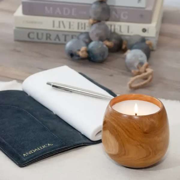 Lit candle beside a notebook and pen on a desk