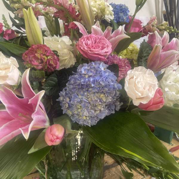 Mixed arrangement of pink lilies, roses, and blue hydrangeas in a clear glass vase