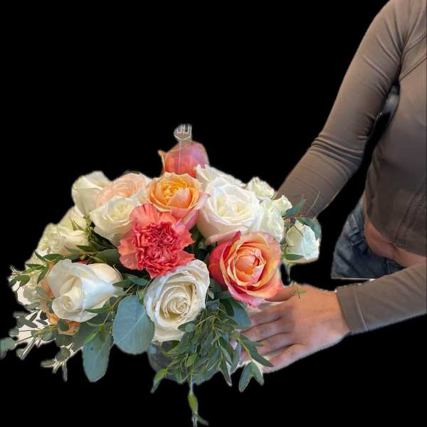 Person holding a low arrangement of white and peach roses with a coral carnation in a clear vase.