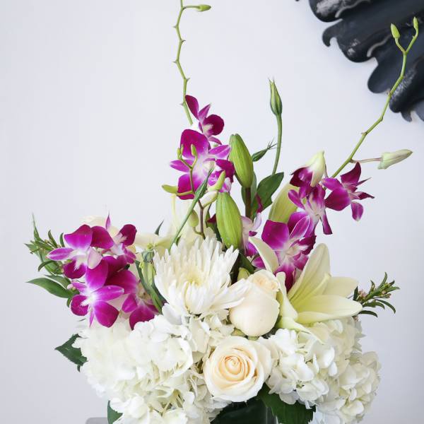 White hydrangeas, roses, lilies, and purple orchids in a green glass cube vase