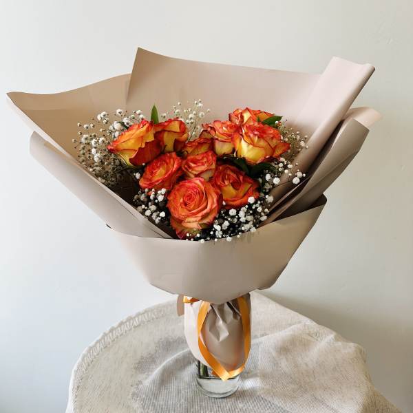 Bouquet of orange-red roses with baby's breath in tan wrapping