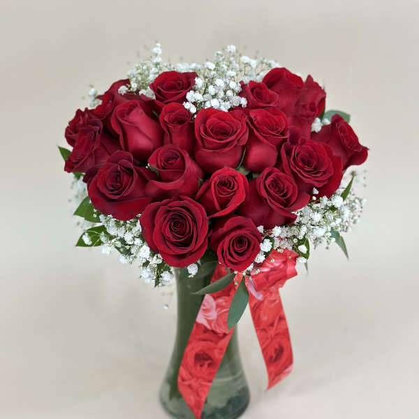 Arrangement of red roses with white filler flowers in a glass vase with a red ribbon