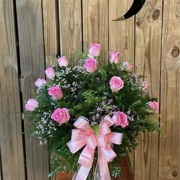 Pink roses arranged in a glass vase with a pink ribbon bow