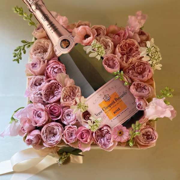 Pink rose arrangement with two champagne bottles in a gift box