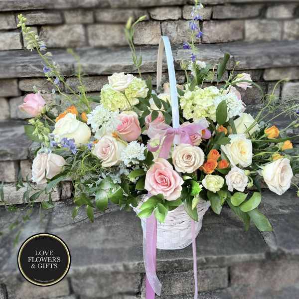 Pastel basket arrangement of roses, hydrangea, and mixed blooms with a pink bow on stone steps