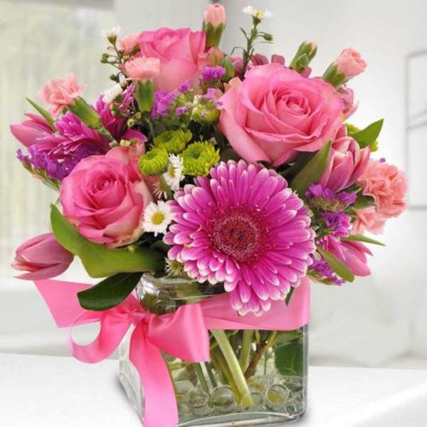 Pink roses and gerbera daisies in a glass vase with a pink ribbon