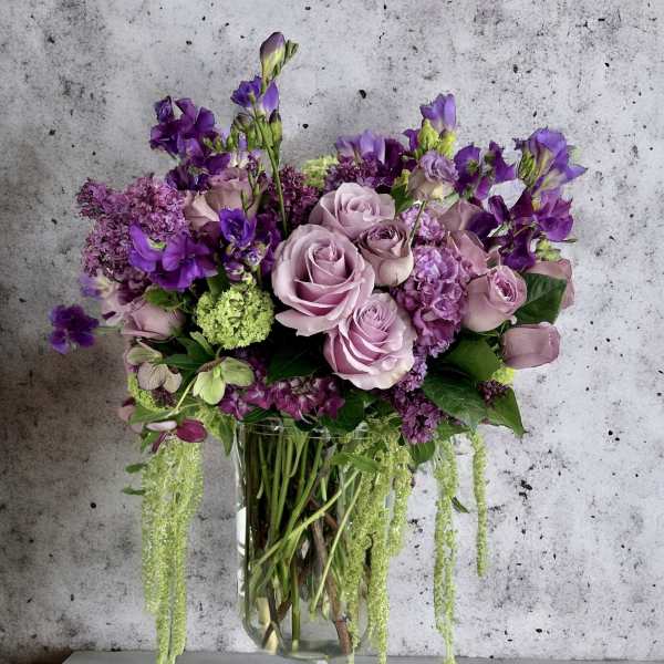 Lavender roses and purple flowers arranged in a clear glass vase