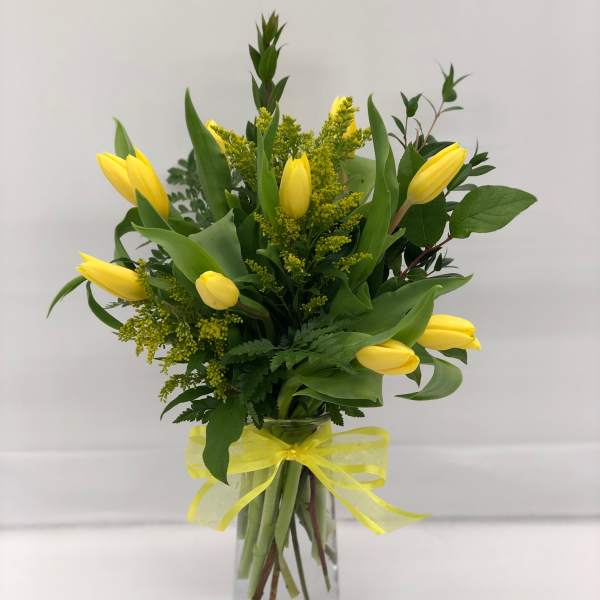 Yellow tulips arranged in a clear glass vase with a yellow ribbon