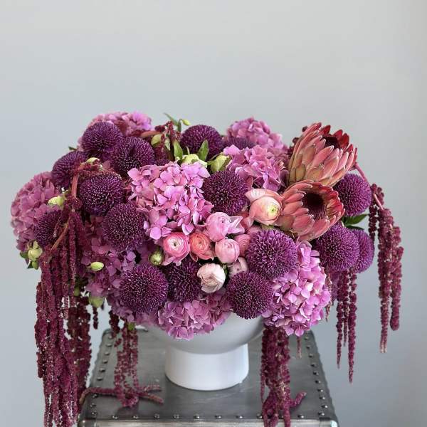 Pink and purple floral arrangement in a white vase with trailing blooms