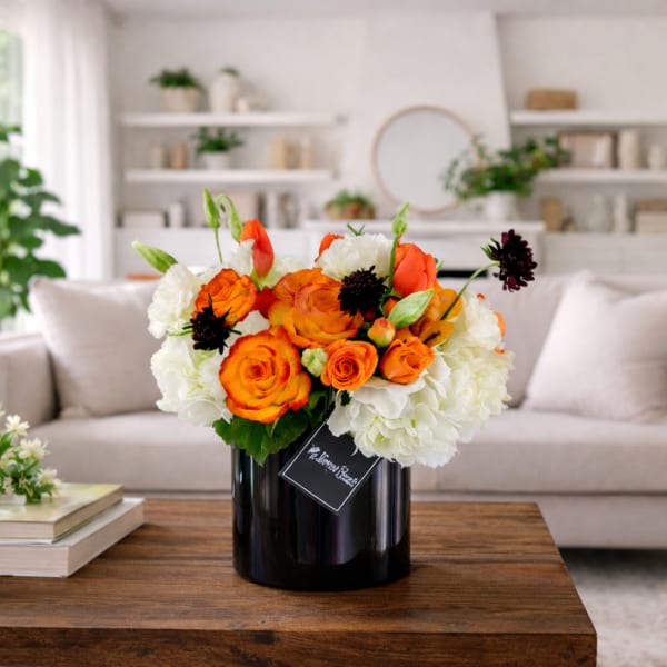 Orange and white flower arrangement in a black vase on a table