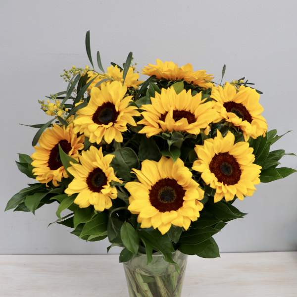 Tall glass vase of bright yellow sunflowers with dark centers arranged in a full bouquet