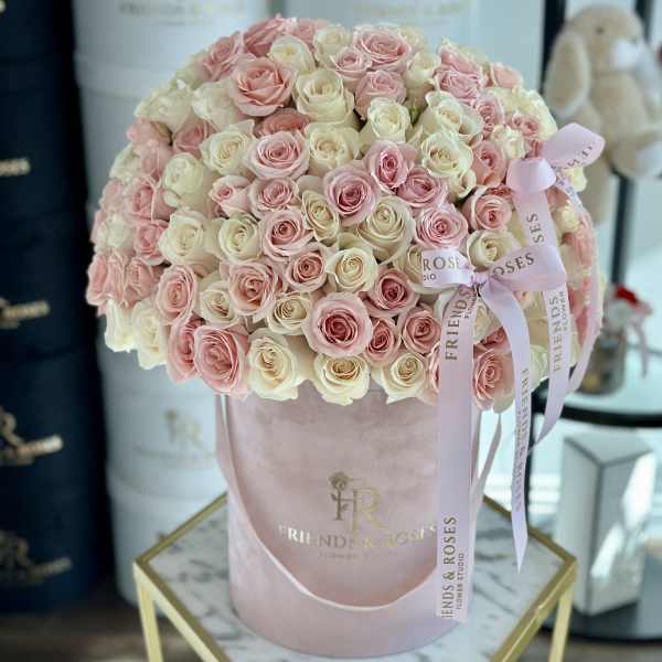 Pink and cream roses arranged in a round blush hatbox with ribbon bows