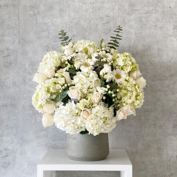White floral arrangement in a gray vase with roses and hydrangeas