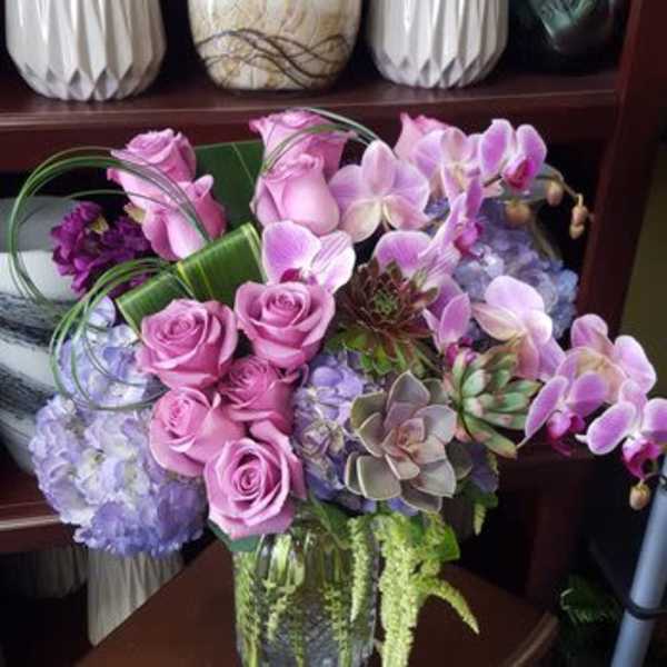Pink roses and orchids arranged in a glass vase with succulents