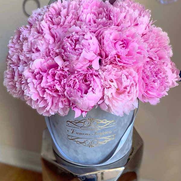 Pink peonies arranged in a gray hat box with a ribbon.