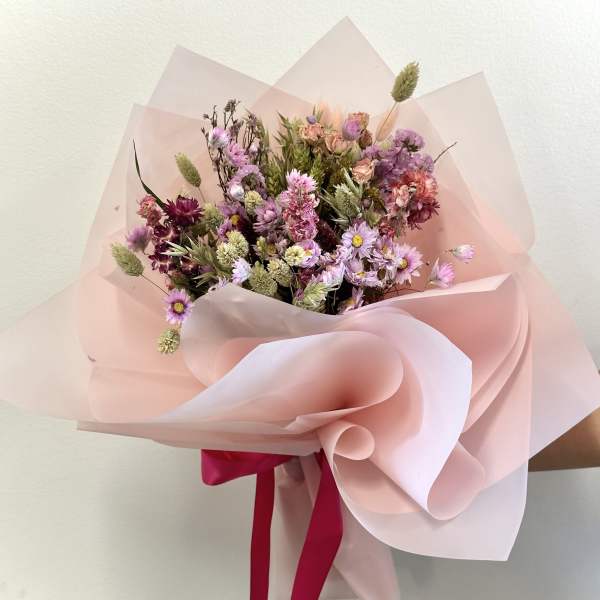 Hand-tied bouquet of pink and purple dried flowers wrapped in pale pink paper