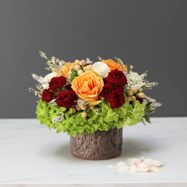 Compact bouquet of red and orange roses in a bark-textured vase