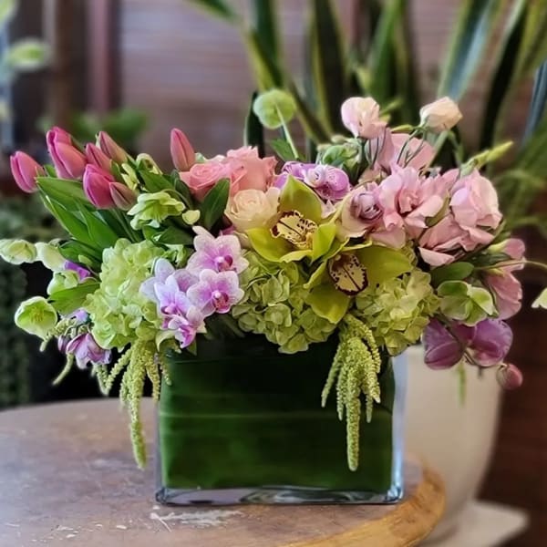 Pink and green floral arrangement in a square glass vase