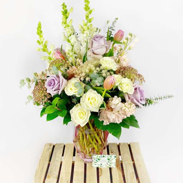 Lavender and white flower arrangement in a pink glass vase