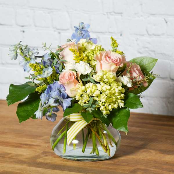 Bouquet of pink roses, blue flowers, and pale green hydrangeas in a glass vase