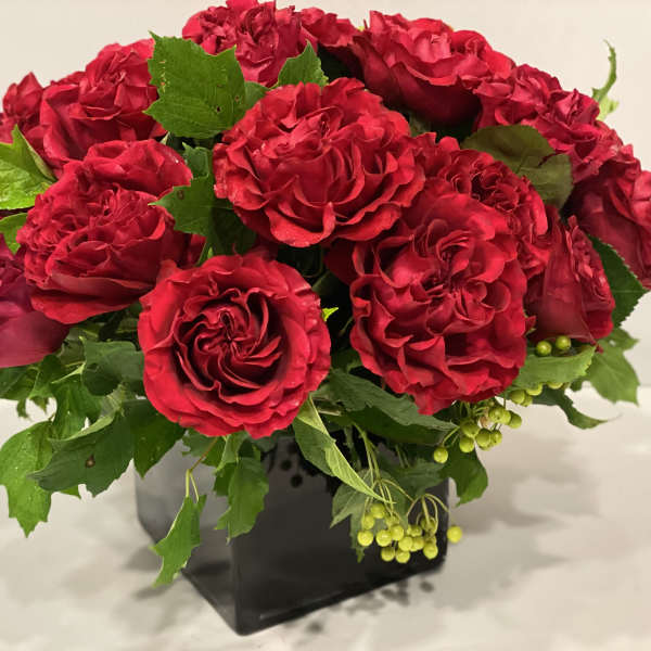 Red rose bouquet in a black square vase with green foliage