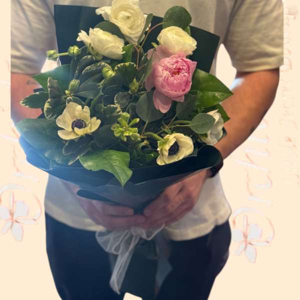 Handheld bouquet of white and pink flowers wrapped in dark paper