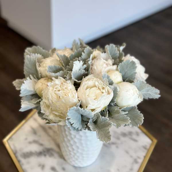 Cream peony bouquet in a white textured vase with silvery foliage