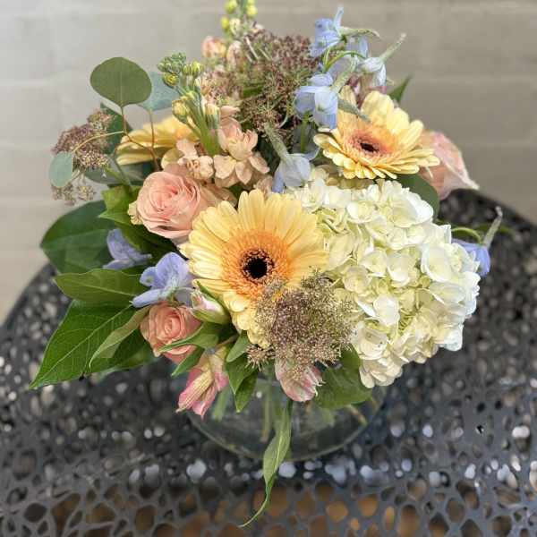 Mixed bouquet with yellow gerbera daisies, pale pink roses, and white hydrangea in a glass vase