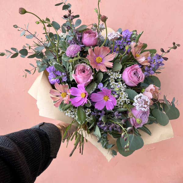 Handheld bouquet of pink and purple flowers wrapped in paper
