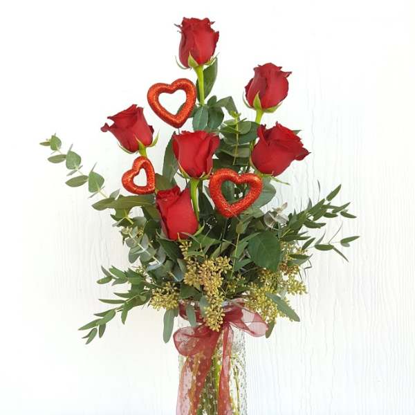 Tall bouquet of red roses in a clear glass vase with heart decorations