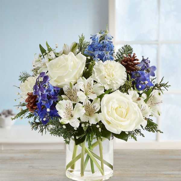 White roses and blue flowers arranged in a clear glass vase
