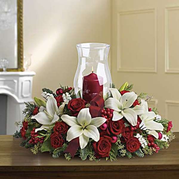 Red roses and white lilies arranged around a red candle in a glass hurricane