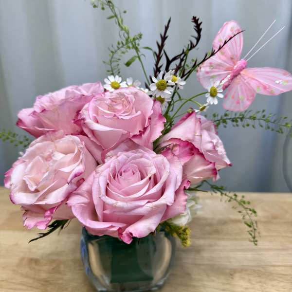 Pink roses in a glass vase with small white daisies and a pink butterfly decoration.