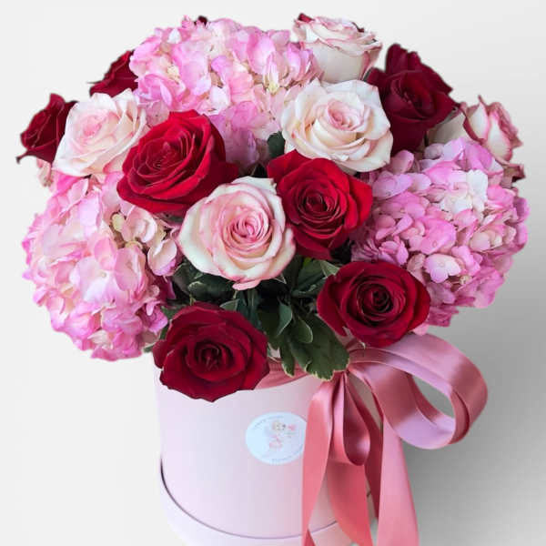 Pink and red roses with hydrangeas in a round pink box tied with ribbon