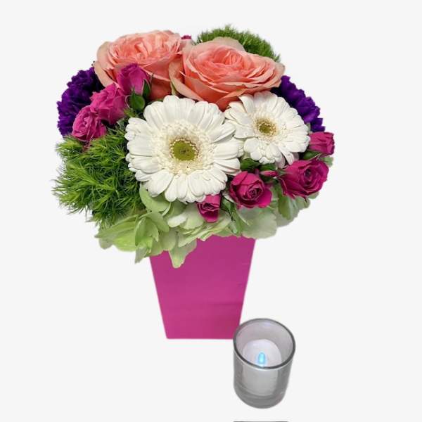 Pink and white flower arrangement in a magenta vase with a candle