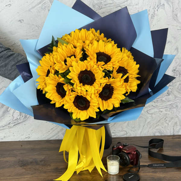 Bouquet of yellow sunflowers wrapped in blue and navy paper with a yellow ribbon