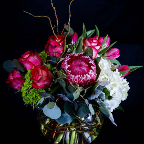 Bouquet of pink roses, a protea, and white hydrangeas in a glass vase